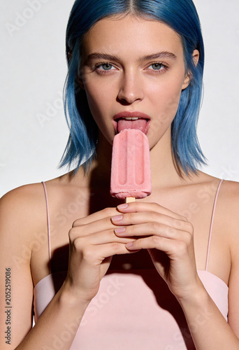 Junge Frau mit blauen Haaren leckt an einem rosa Eis am Stiel
