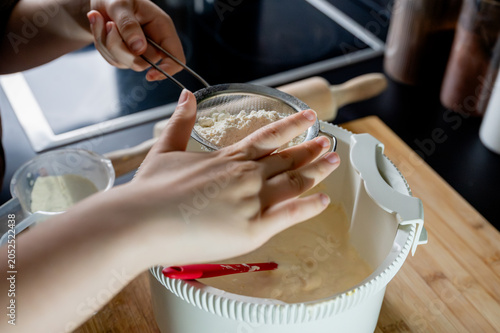 Canvastavla Close-up of hands sifting flour through a sieve into a bowl of sponge cake batter in a modern kitchen adding dry ingredients for a homemade cake