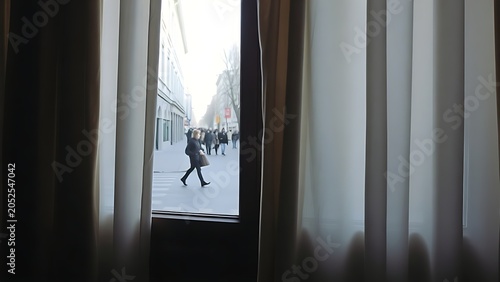 A view through parted curtains onto a quiet street with occasional passersby.