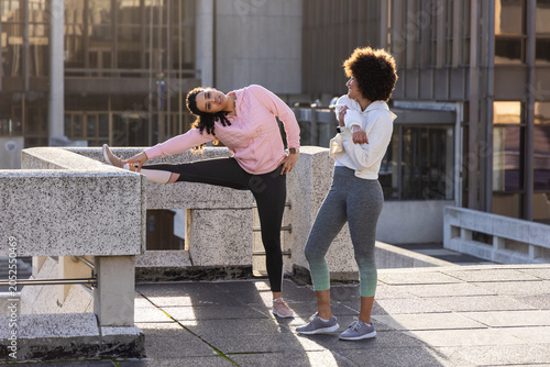 Bilde på lerret Diverse female friends stretching and chatting in hoodies on rooftop using parap