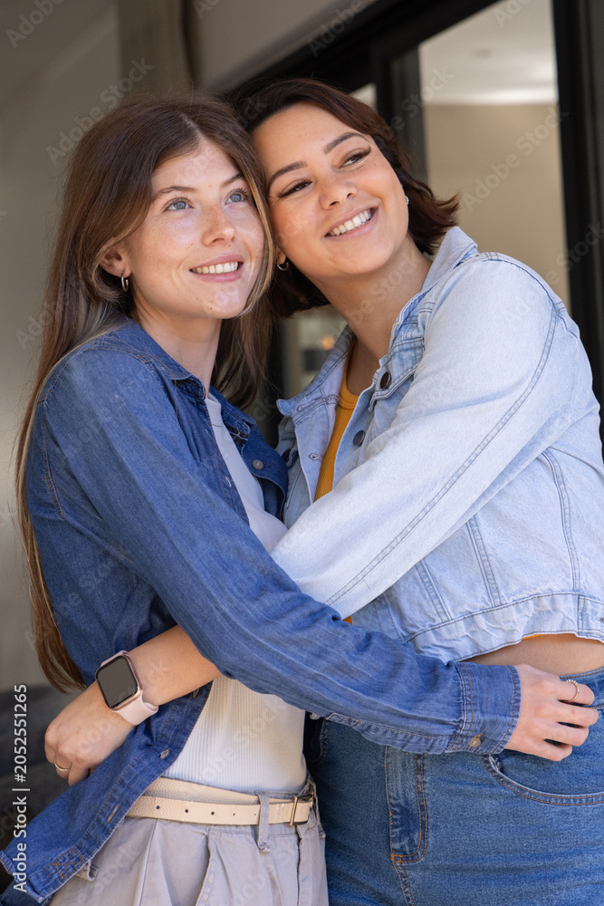Obraz premium Diverse female partners embracing and smiling at doorway in denim near sliding door with smartwatch