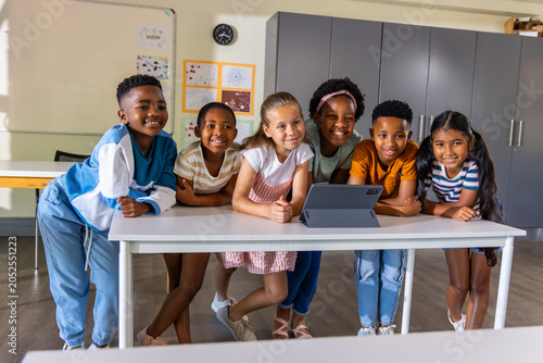 Vászonkép Diverse school-age classmates leaning and watching tablet propped on folio at cl