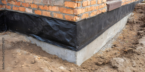 The corner of the brick foundation for a new or existing home features an exterior waterproofing membrane applied over the concrete base. A black protective layer prevents water and moisture from caus