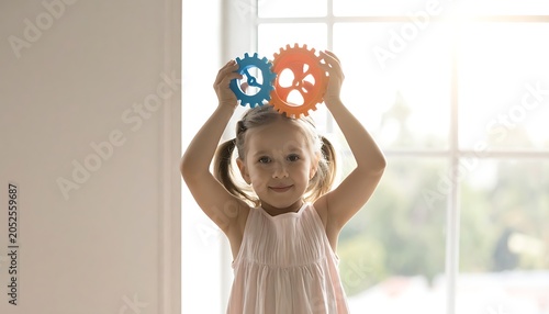 Young girl holding colorful gears up above her head, smiling in front of a window with bright background