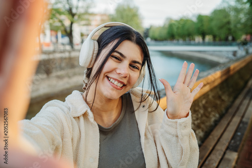 Woman with headphones waving hand during selfie video call