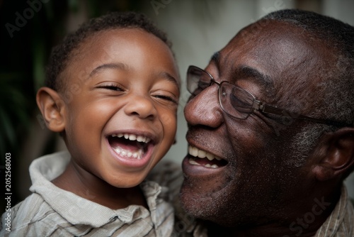 Diverse grandfather holding his grandson outdoors, both smiling and laughing with focus on joyful faces. Intergenerational love, happy family moment in natural light. Grandad.