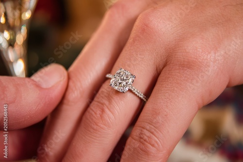 Close-up of hand wearing sparkling lab-grown diamond engagement ring with cushion cut, being shown off at engagement party. Celebration, modern proposal.