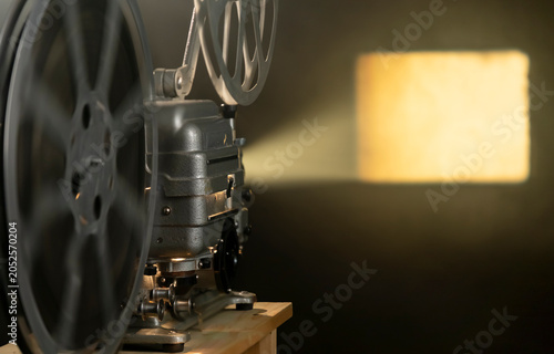 Vintage film projector plays classic movies in a dimly lit room with a bright beam of light shining on the wall