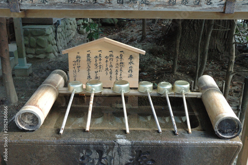 Traditional water purification pavilion (Chozuya) at a Japanese Shinto shrine with metal ladles and a wooden sign explaining the etiquette, Sendai, Japan.