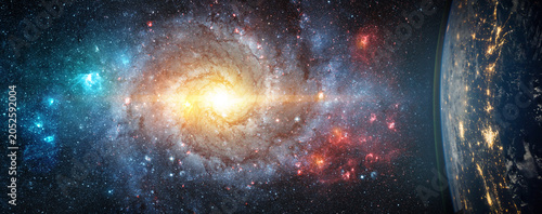 Tableau sur toile Spectacular deep space scene featuring a luminous spiral galaxy surrounded by billions of stars and colorful nebulae, viewed alongside Earth from orbit