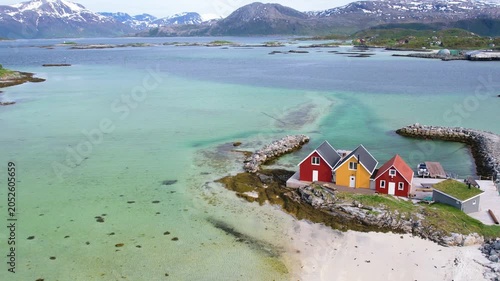 Aerial of small traditional rorbu fishing huts with snow covered mountain background on summer Sommaroy island Norway