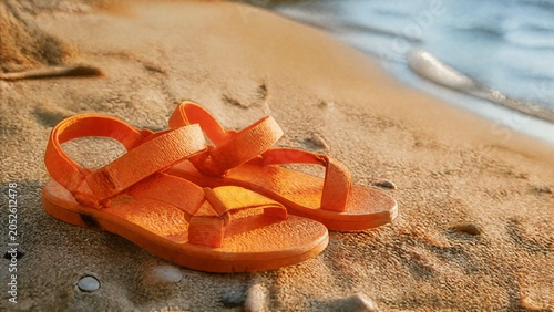 Bright orange sandals resting on a coastal shore, bathed in warm sunlight with a soft beach atmosphere.