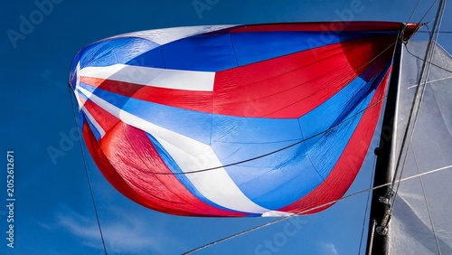Colorful spinnaker sail billowing in strong wind against a clear sky.