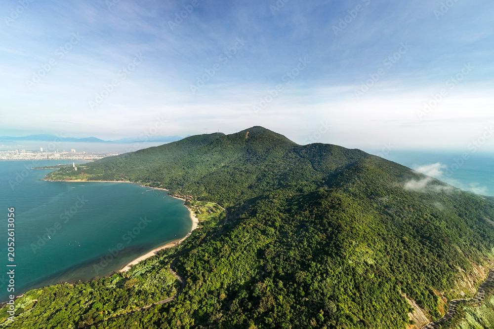 Obraz premium An aerial view shows the Son Tra Peninsula in Da Nang, Vietnam, with its densely forested mountain slopes meeting the clear blue ocean and a sandy beach