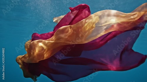 Red and gold fabric flowing gracefully in deep blue water