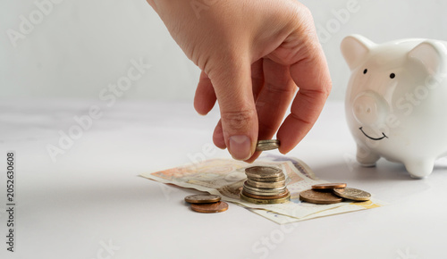 Tableau sur toile Hand placing coin near piggy bank with cash money, saving investment budgeting a