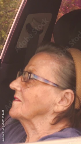 Old woman driving a car in the countryside, road trip concept.  Portrait of an old woman driving and near a car, on a walk outside the city. Vertical, vertical video.