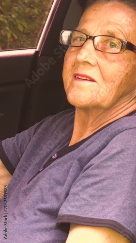 Old woman driving a car in the countryside, road trip concept.  Portrait of an old woman driving and near a car, on a walk outside the city. Vertical, vertical video.