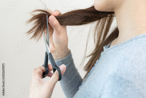 Hair problem person, frustrated asian young woman, girl use scissors to trim off the damaged of hair, heat damage and dry hair, split ends and hair texture thinning. Healthcare of beauty concept.