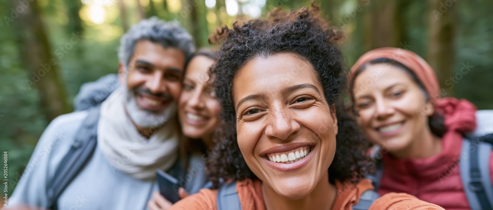Fototapeta premium A diverse group of four friends, smiling and hiking in a beautiful forest, exemplifying friendship, adventure, and the joy of exploring nature together, creating lasting memories.