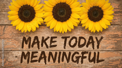 Three beautiful sunflowers on a rustic wooden background with the inspirational text make today meaningful written in dark brown letters