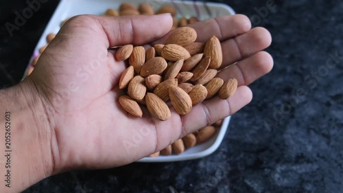 Hand holding a handful of fresh raw almonds with a bowl in the background