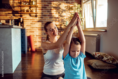 Smiling mother helping daughter with yoga pose at home