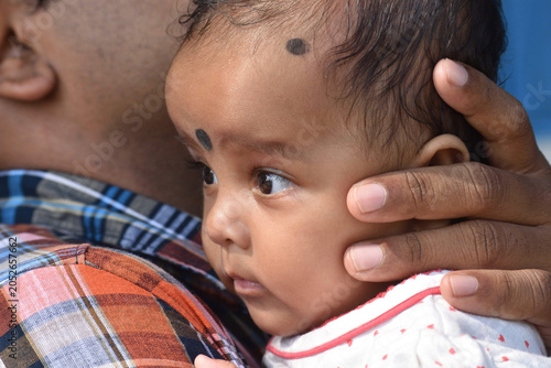 An Indian little girl hugs father, eyes soft and trusting, close up. She looks up, curious, with warm, gentle expression. Family, parenting, Fathers day concept.