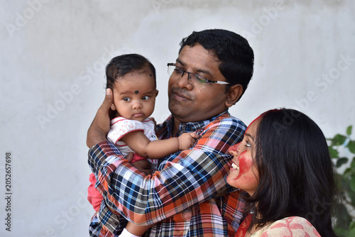 Indian young happy father and mother with four months old baby girl spend time together hugging and cuddling smiling embrace cute little child love concept.