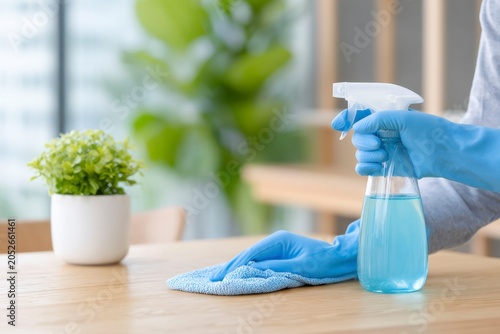 a person wearing blue gloves is cleaning the table with a rag and water spray bottle, in a cafe interior background