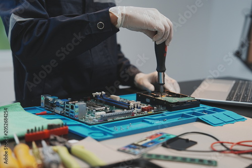 Fotografie A technician wearing white gloves uses a screwdriver to assemble or repair a hard drive placed on a blue silicone work mat
