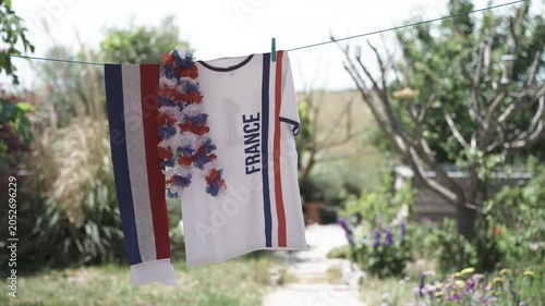 Soccer fan shirt, scarf and leis in national colors of France hanging outdoors in garden on clothesline on sunny windy day
