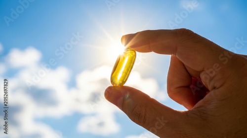 Vitamin D from the sun helps maintain health as a hand holds a fish oil capsule in sunlight.
