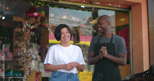Two small business owners laughing together outside flower shop, joyful interaction and positive energy, floral background and friendly atmosphere