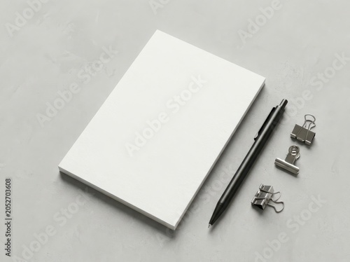Blank white notepad with a black pen and metal clips on a gray surface