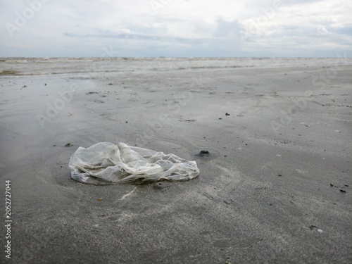 Discarded plastic bag on a sandy beach, marine pollution concept.