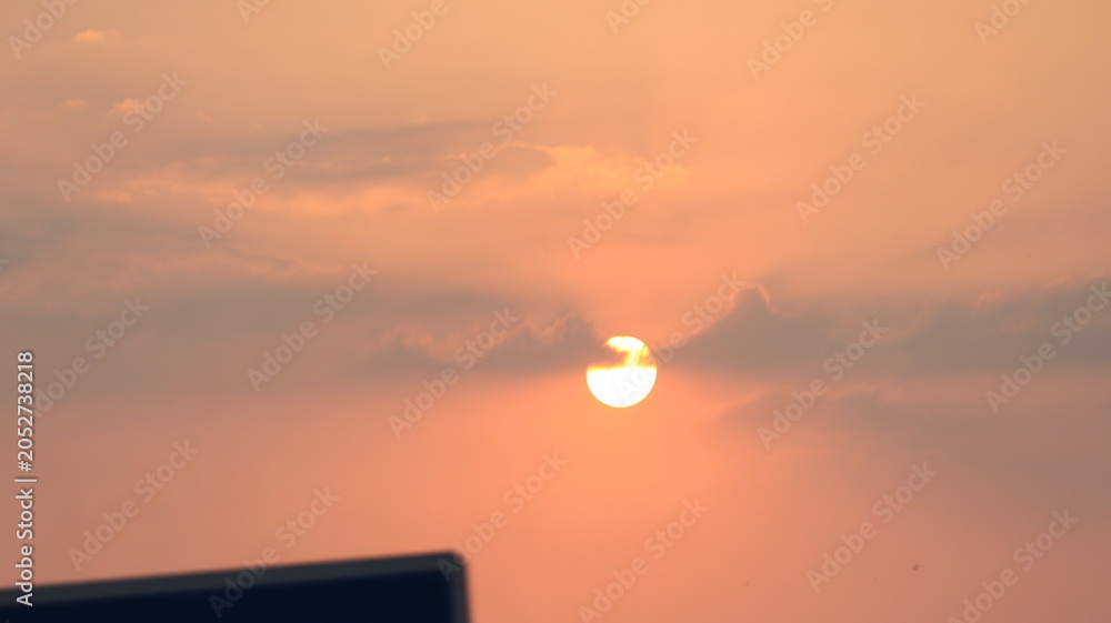 Fototapeta premium Dreamy orange sunset with glowing sunlight and layered clouds creating a relaxing sky view.
