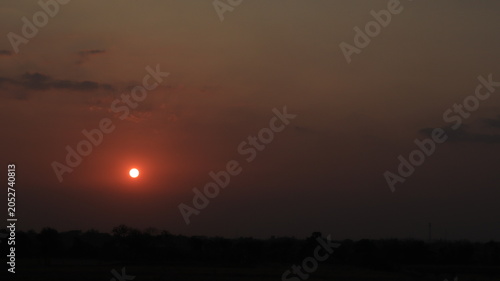 Foto Bright evening sun glowing over distant fields and trees beneath a warm orange sky