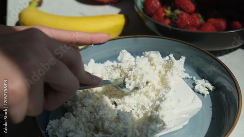 Hands using fork to loosen dairy cottage cheese in plate for eating. Fat free premium cottage cheese for breakfast with sour cream and sweet topping. Fresh natural dairy products. Fermented milk food
