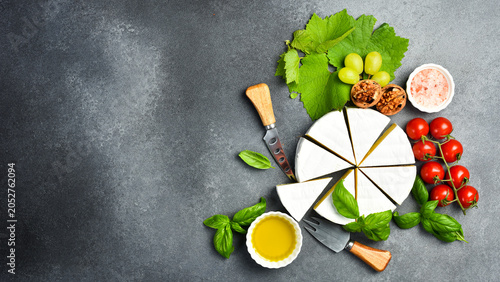 Delicious Brie cheese cut into slices, served with basil and spices. On a stone background. Cold appetizers.