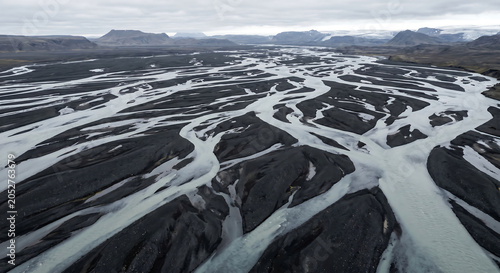 Aerial wide angle shot of silty braided river channels winding through dark volcanic sand