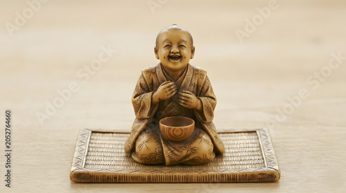 Laughing monk statue sitting on a wooden mat with bowl  