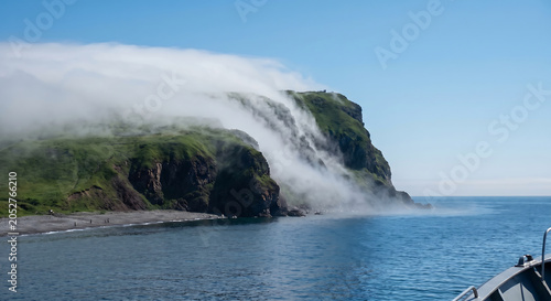 Sea fog pouring over coastal headland cliffs like a slow waterfall. Heavy mist and low clouds cascading down a green coastal cliff into the ocean. 