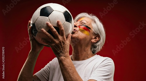 Elderly German Woman Fan Kisses Soccer Ball with National Flag Face Paint
