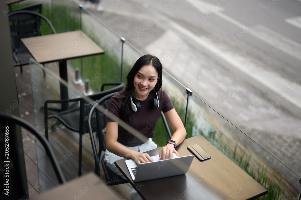 Fototapeta premium Smiling young woman typing on laptop at outdoor cafe