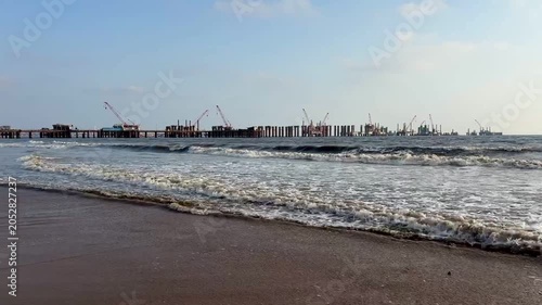 Coastal bridge construction site on sandy beach with sea waves