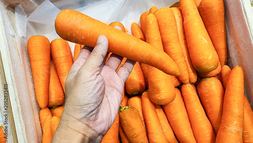 Quadro em tela A top-down shot of fresh, bright orange carrots arranged neatly in a wooden crate at a supermarket display counter