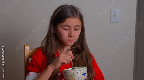 Young girl eating a home cooked meal from a patterned ceramic bowl, occasionally giving a funny look to the camera. 