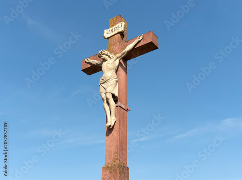 Photos Stone statue of Jesus Christ crucifixion affixed to a large cross with visible texture and a slightly weathered appearance