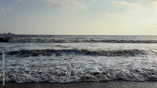 Splashing sea waves with white foam on sandy beach shore
